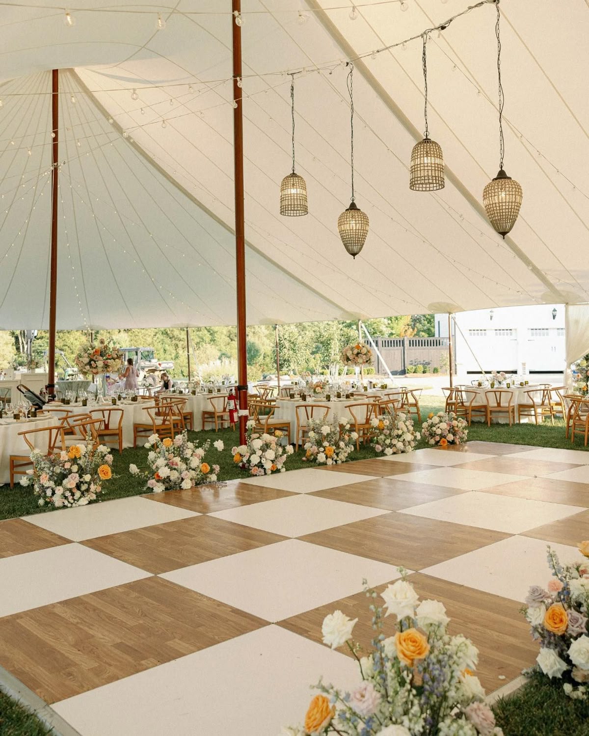 “Tented wedding reception in Wilmington NC with checkered dance floor, hanging lanterns, and lush neutral floral arrangements.”