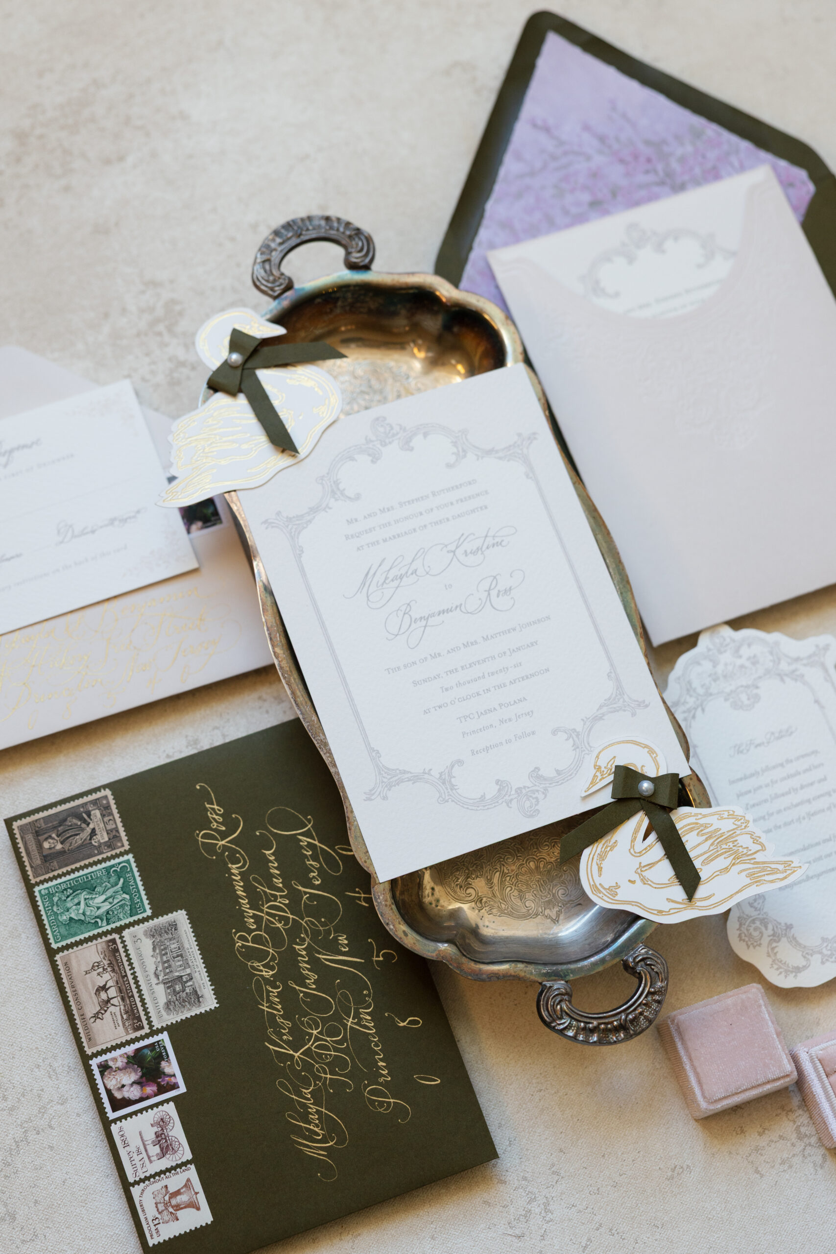 Luxury wedding invitation suite with calligraphy envelopes, vintage postage stamps, wax seals, and soft neutral paper textures styled on an antique silver tray.