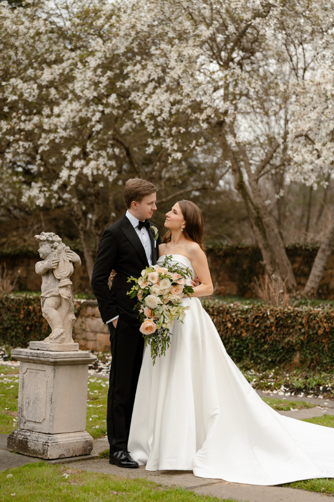 Bride and groom posing with cascading bridal bouquet in a blooming garden at a luxury wedding venue.