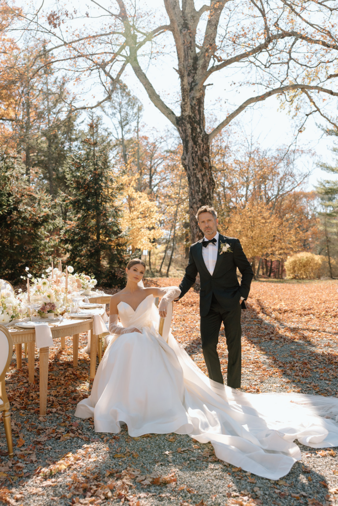 Bride and groom posing together beneath autumn trees during an outdoor wedding