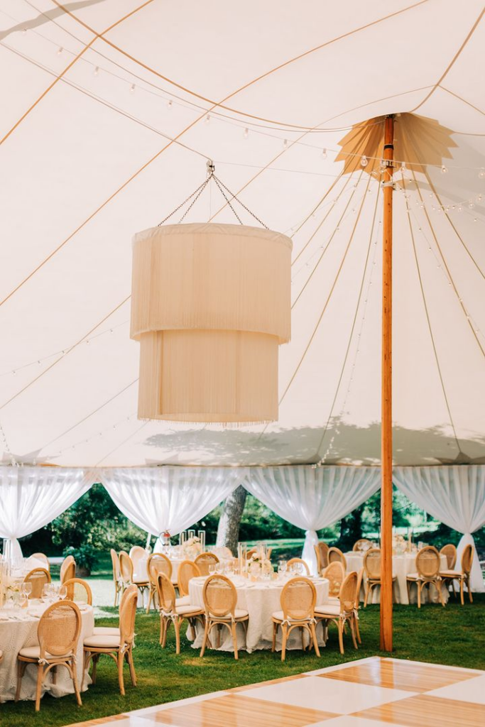 Elegant sailcloth wedding tent with a wooden dance floor and round guest tables set for a luxury outdoor wedding reception.