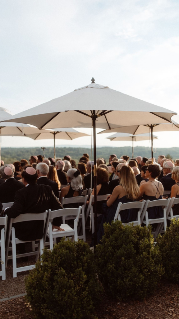 Outdoor wedding ceremony with guests seated beneath large white umbrellas overlooking the landscape